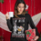 Woman wearing a black Christmas sweater with a milk bottle and a cookie character on it, holding a white mug, smiling, and looking at the camera.