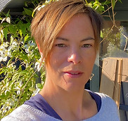 Woman with short hair - Emma Pyle - smiles for camera, outdoor background with green foliage.