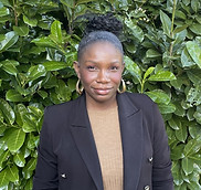 Smiling woman - Lena Norman - in a black blazer stands in front of green foliage.