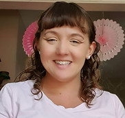 Smiling woman - Holly Moore - in a pink shirt with pink paper decorations in background.