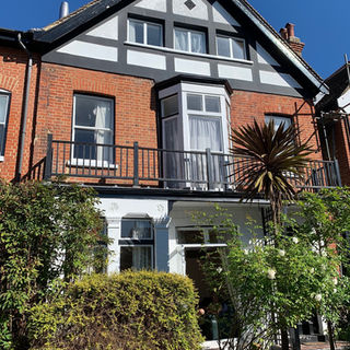Red brick house with white trim and balcony on a sunny day - view of Richmond House from street