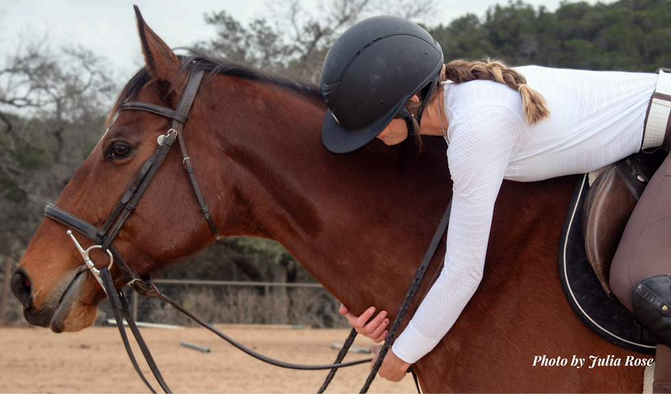 Rider in black helmet hugs brown horse at a sandy arena; saddle and reins visible, with Photo by Julia Rose watermark.