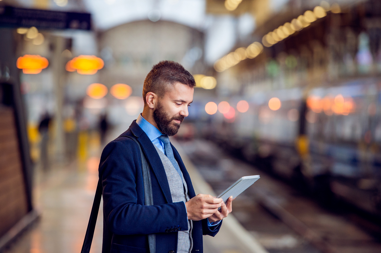 A man in a suit, reading his tablet whilst waiting for a train