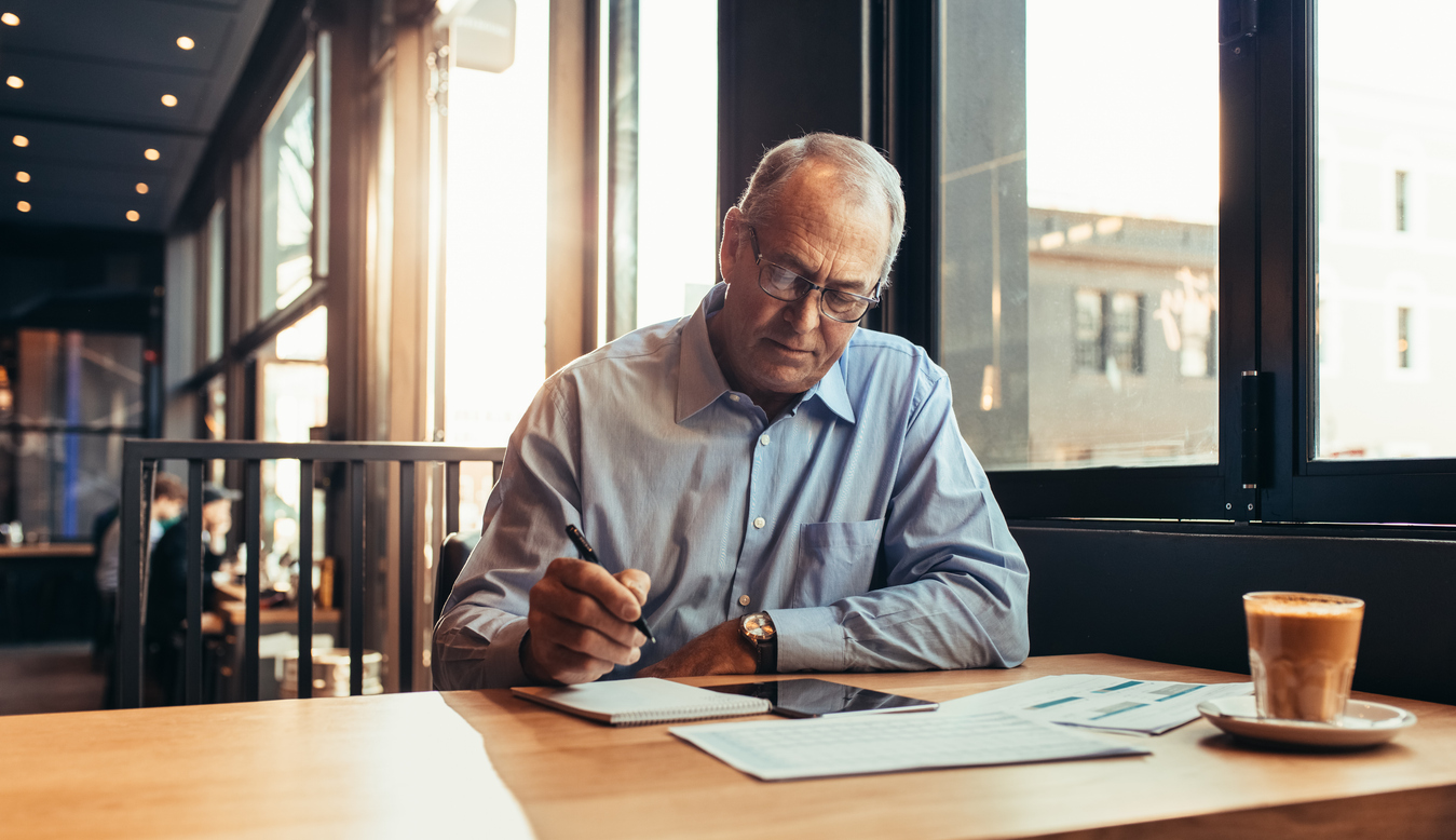 Image of a man writing notes on a paper writing pad.