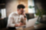 A man in glasses, looking into his lap which is sat on a desk.   The man is typing into his laptop whilst looking happy with what he's reading