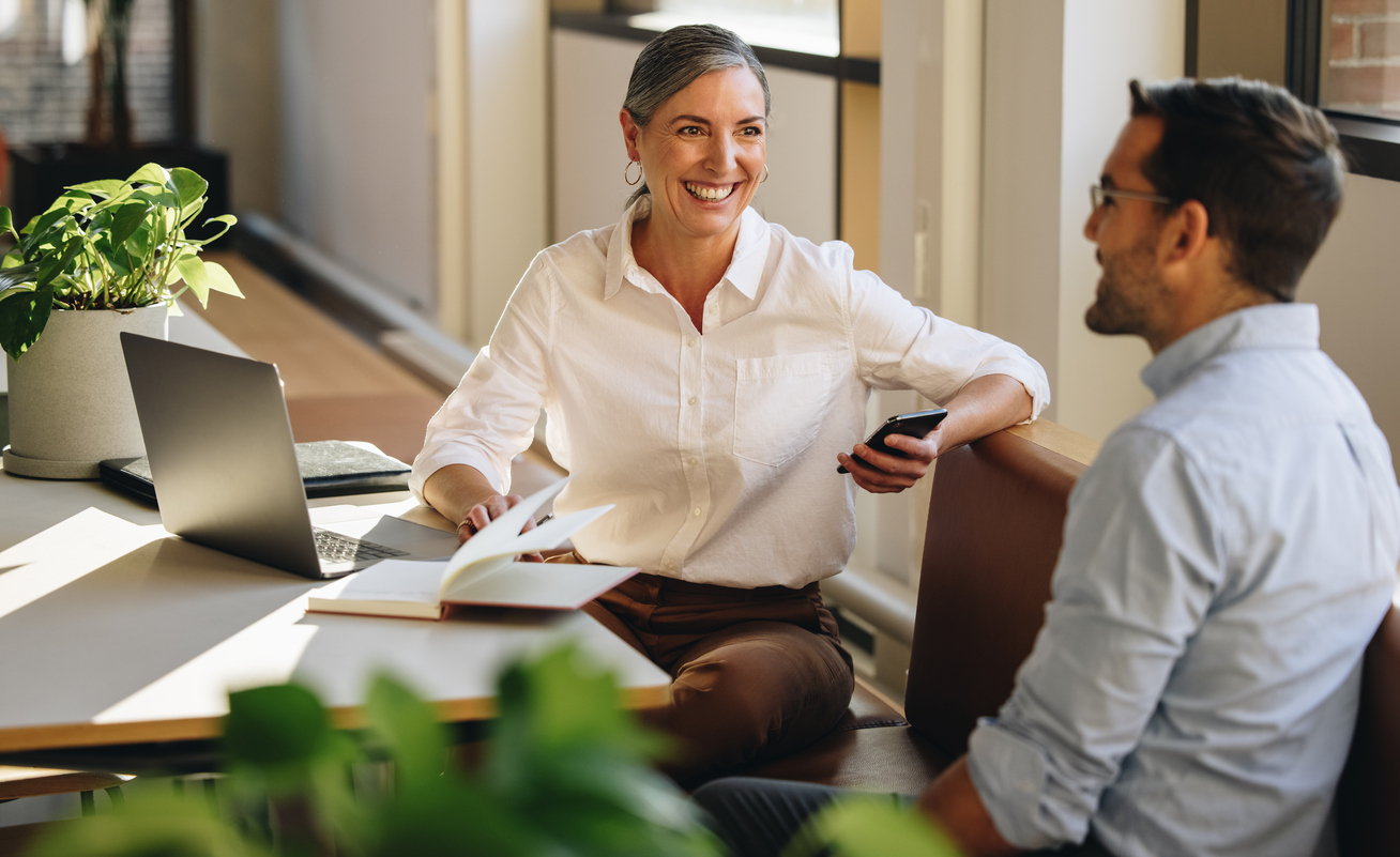 Woman sat with man, conversing whilst at work.