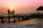 Silhouetted family walks on a pier at sunset over the ocean, sky glowing in pink and orange hues, creating a serene and warm mood.
