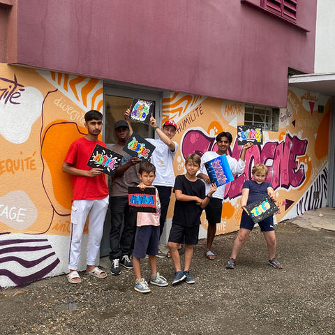 Groupe de jeunes présentant leurs réalisations devant une fresque murale participative terminée