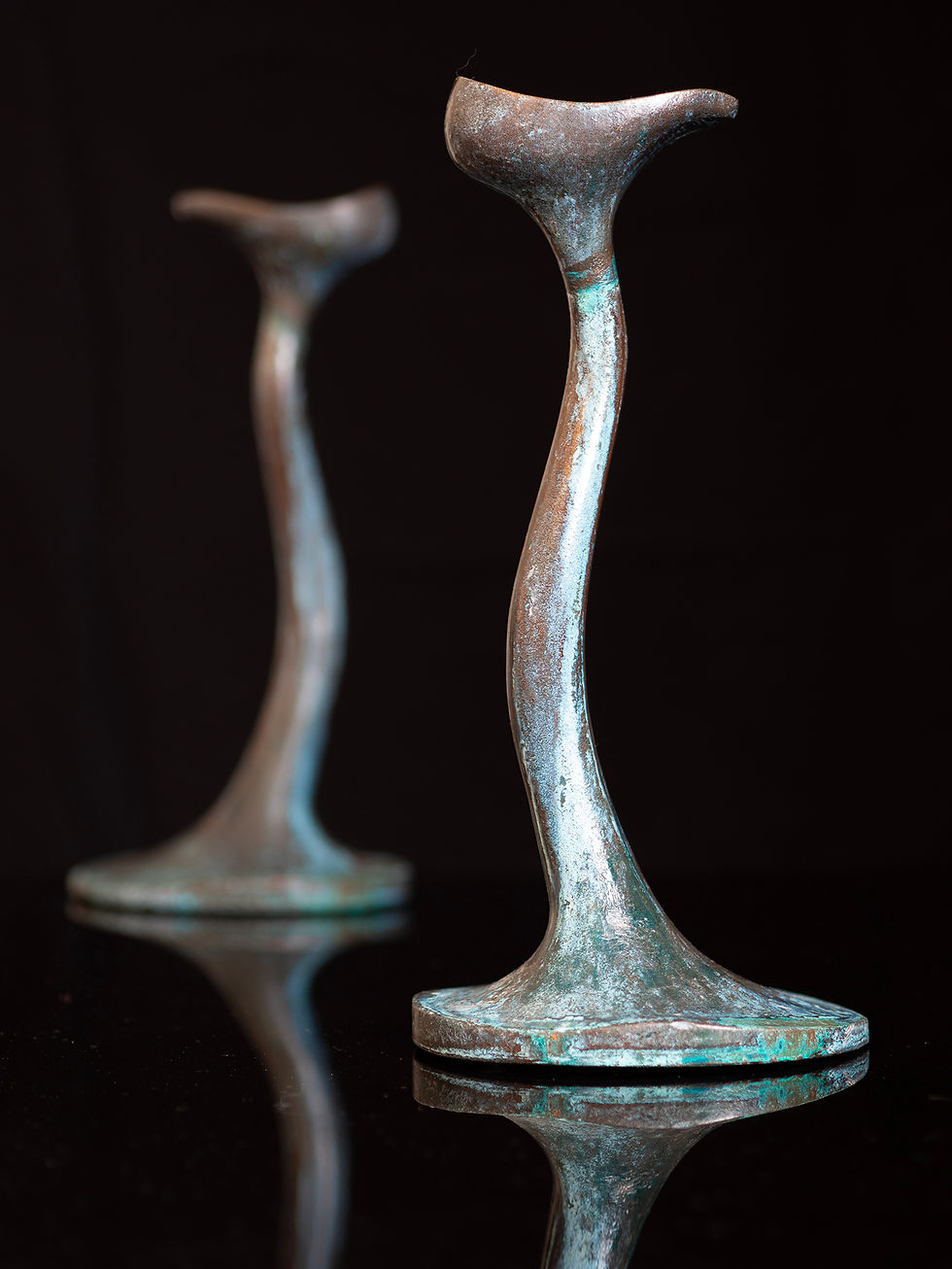 a pair of tall candlesticks of organic, flowing form cast in verdigris bronze