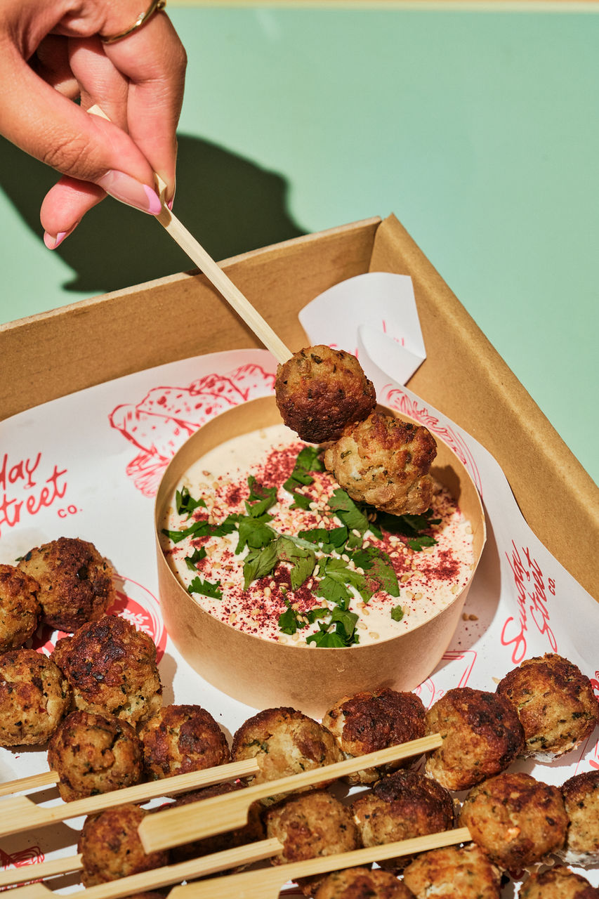 Crispy meat skewers dipped into creamy tahini sauce with herbs
