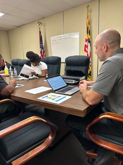 Man leading professional meeting at table with Maryland flag in background