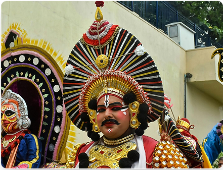 A man in a colorful traditional costume poses with ornate headwear and makeup.