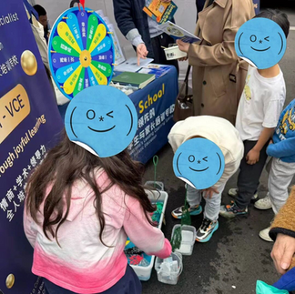 Children play with toy sea animals in a blue water tub, using nets. The scene is outdoors with banners and QR codes in the background.