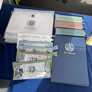 Colorful prize wheel with Chinese text at a booth. Background has brochures and leaflets titled "DRABBLES" on a table with a blue cloth.