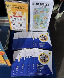 彩色幸运转盘上有奖项,背景是宣传资料和杂志,桌布上有Qs School标志,整体风格活泼吸引人。