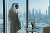Executive coach Saeed Alghafri wearing a white Kandura and Ghutra, looking out a tall glass window onto a cityscape