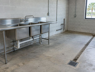 Three-compartment sink and floor drain in an empty commercial kitchen shell