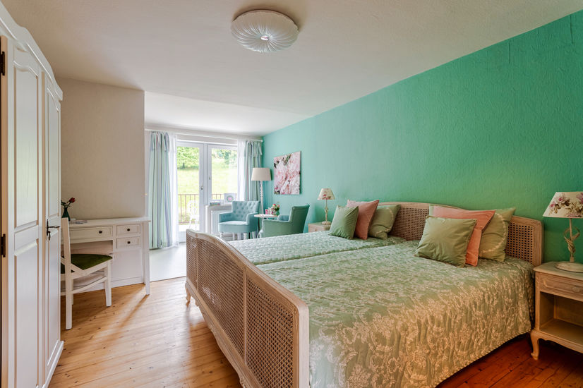 Großes Doppelzimmer mit einer hellen Terrasse hintenraus. Rosenlampen auf den Nachttischen und rosa, sowie türkisfarbene Kissen auf den Betten.
