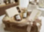 Packshot photography of a luxury gift basket. It contains gourmet chocolates, olive oil, nuts, a scented candle, notebook, and pen, beautifully presented with a ribbon, evoking an upscale and thoughtful gift.
