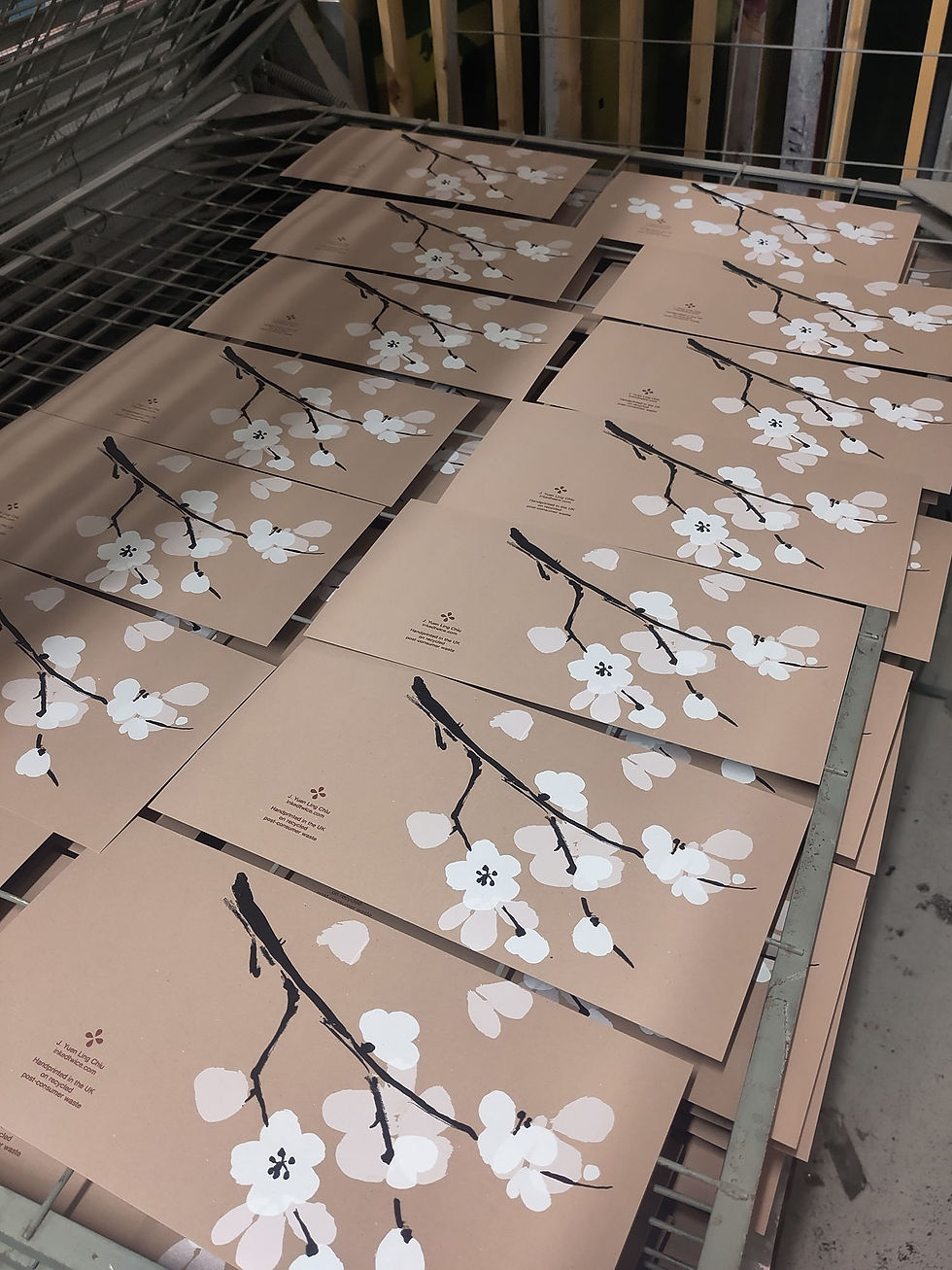 A collection of printed cards of cherry blossom on brown paper drying on a rack