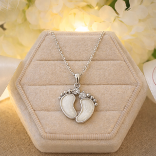 A silver pendant depicting babys feet filled with a milk diamond