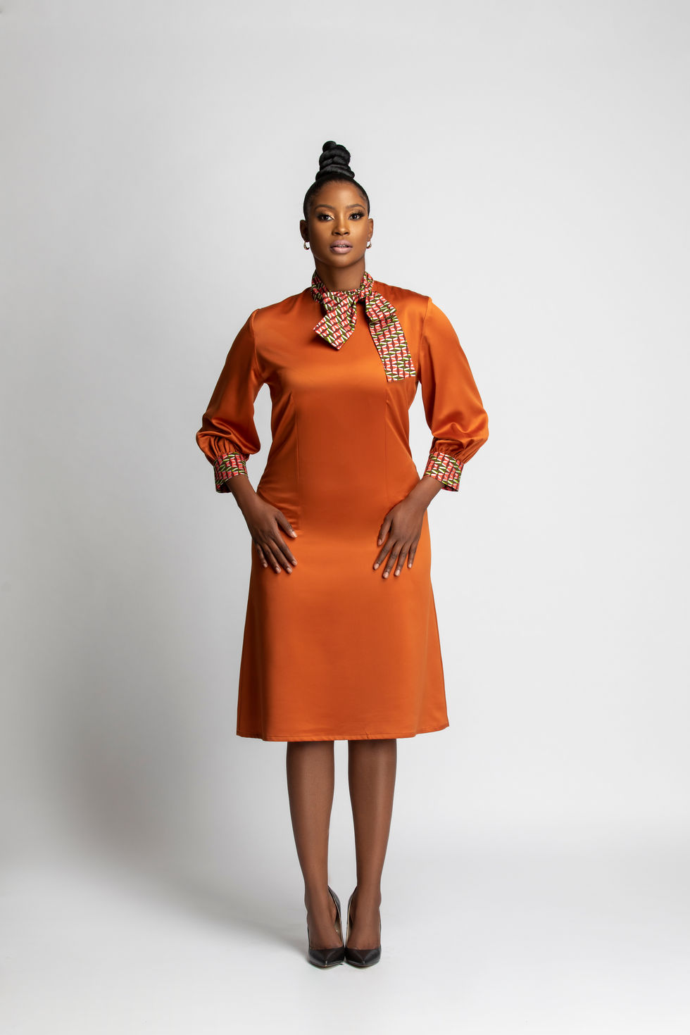 Model wearing an orange satin long-sleeved dress with wax print detailing