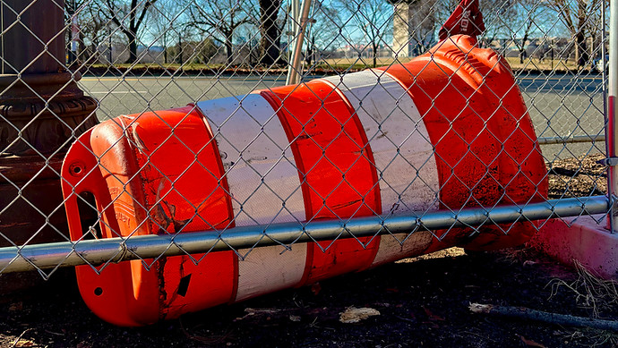 A tipped over drum cone behind a chain link fence.