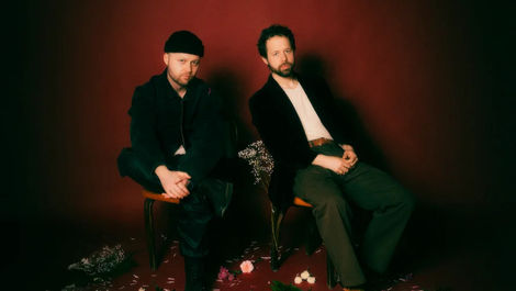 two man sitting in front of a red backdrop 