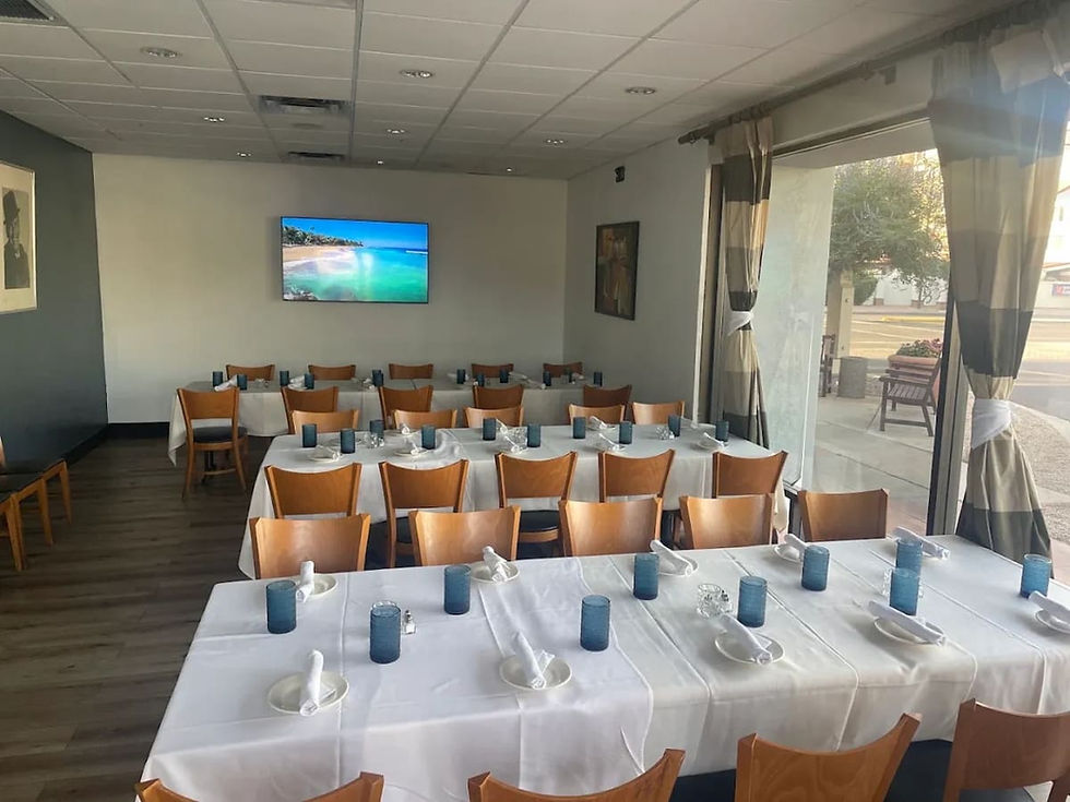 Private dining room at Tommy V's Urban Kitchen & Bar with long tables in white linens, a wall-mounted TV and curtained windows