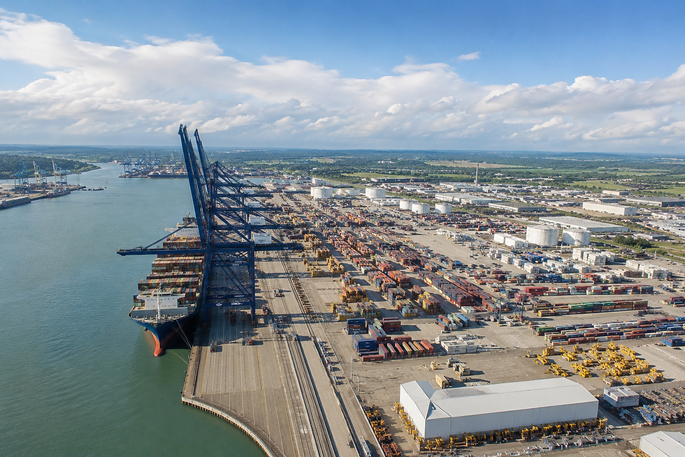 Aerial view of a container ship at a busy port with tall blue cranes, stacked cargo containers, and a cloudy sky.
