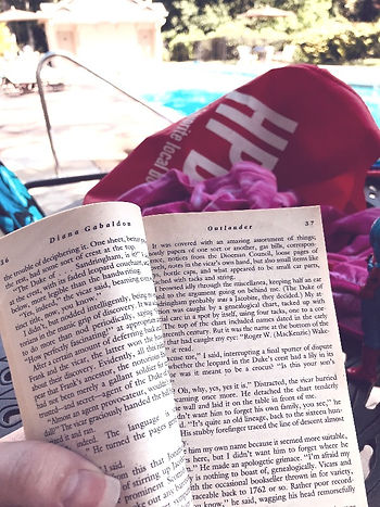 Paperback book held open. In the background, a swimming pool.