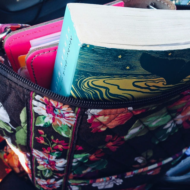 A teal book and a hot pink Filofax peek from a floral print puse.