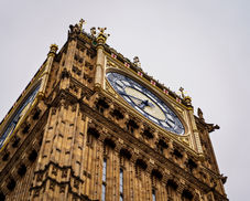 Zbliżenie na jedną z czterech tarcz słynnego zegara w Wieży Elżbiety (potocznie: Big Ben), ukończonej w 1859 roku jako część neogotyckiej przebudowy Pałacu Westminsterskiego. Złocenia, symbole heraldyczne i maswerkowe detale to dzieło Augusta Pugina. Widok od północnego zachodu, z wyraźnie widoczną dekoracją narożną i krzyżem św. Jerzego.