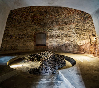 Wnętrze średniowiecznego donżonu Zamku Lubelskiego z ceglanymi murami, wąskim oknem i żelaznym łańcuchem leżącym na posadzce, symbolizującym dawne więzienne przeznaczenie tego miejsca.