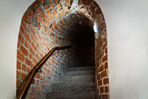 Wąska ceglasta klatka schodowa w donżonie Zamku Lubelskiego o gotyckiej konstrukcji prowadząca na wyższe kondygnacje i podkreślająca obronny charakter wieży.