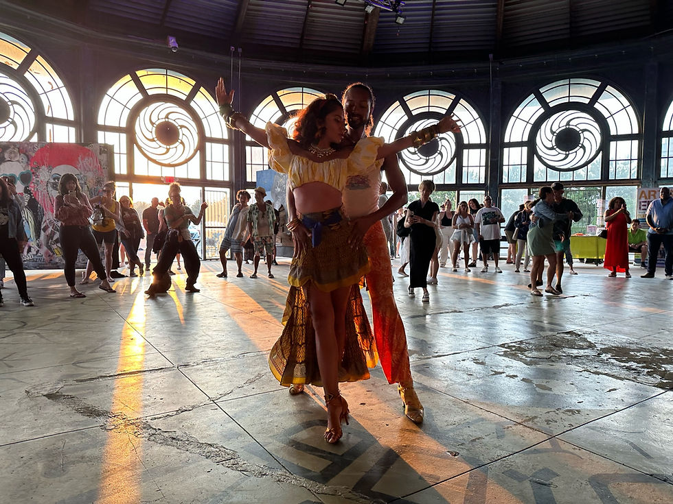 A couple dancing the hustle along with other dancers in the background, inside an old, historic carousel building.