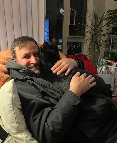 Burak sitting on a couch holding a black cat smiling into the camera