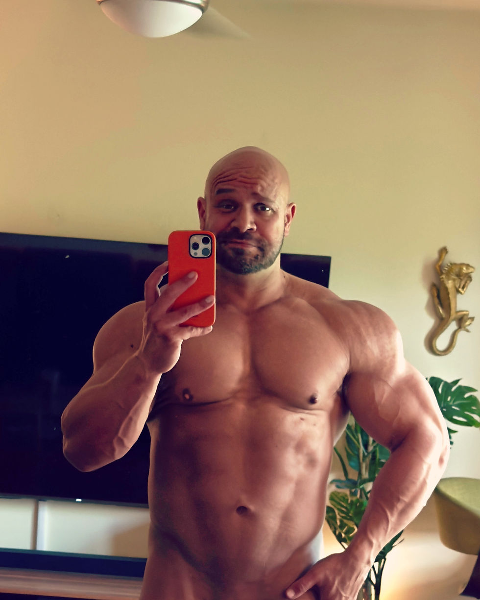 Muscular bald man taking a mirror selfie, showing off a powerful, aesthetic physique built through sex appeal fitness training.