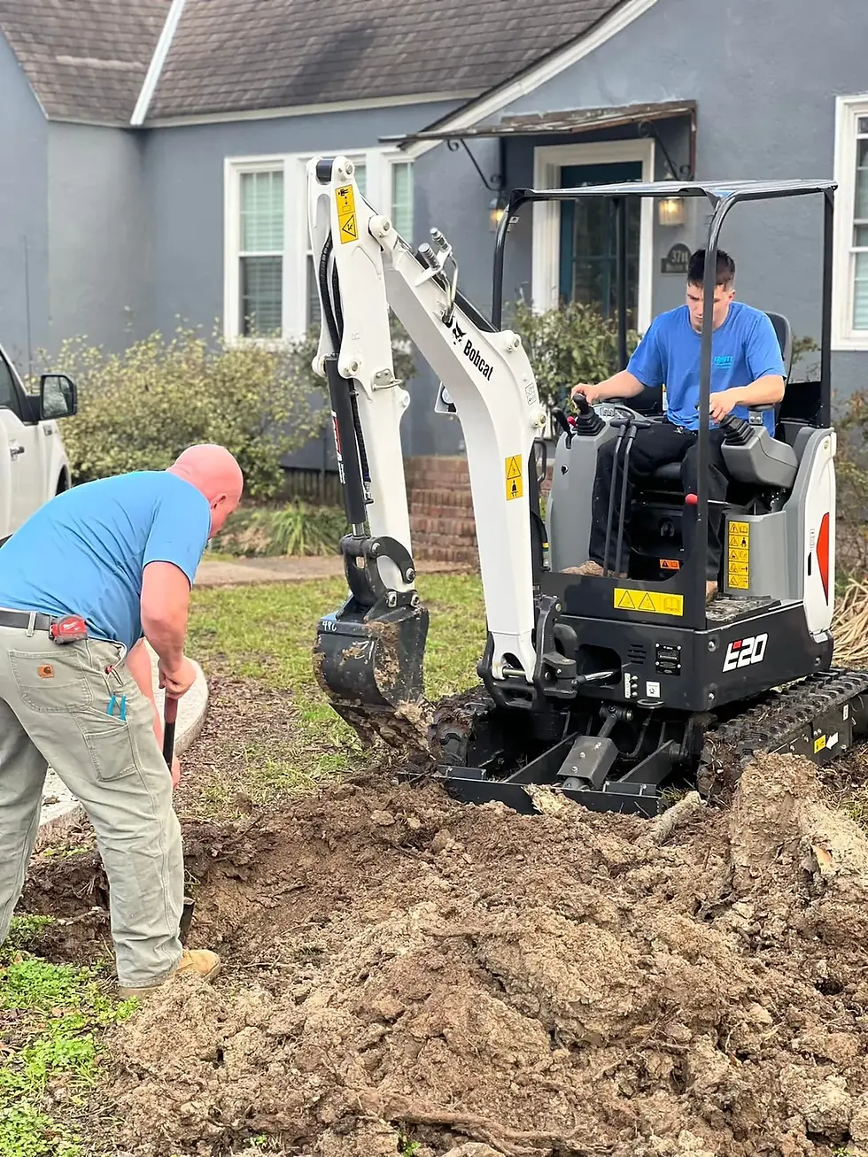 Mini excavator and crew opening a residential yard trench for underground drainage work