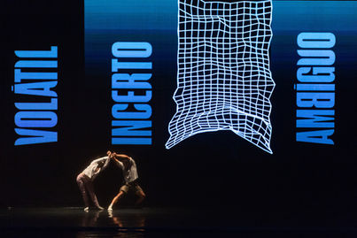 Dançarinos em cena com projeção de 'Volátil, Incerto, Ambíguo'