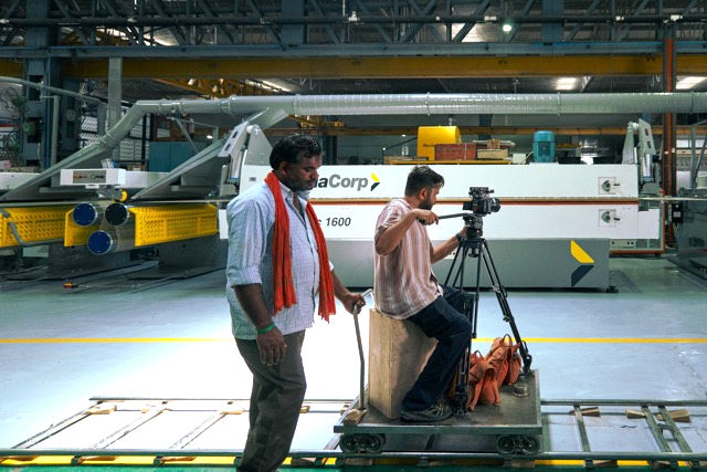 Film crew shooting a corporate film on a factory floor with an overhead crane