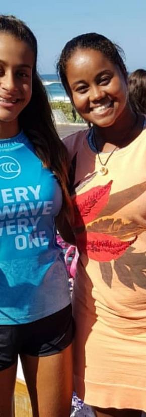 2 garotas uma de camisa azul e a outra de vestido curto em um evento de surf.