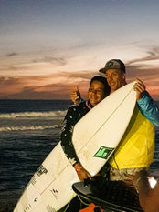 Surfista abraçando a prancha branca com seu pai no entardecer da tarde.