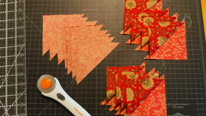 Fabric triangles with floral patterns on a black grid cutting mat. A rotary cutter and measurement lines are visible.