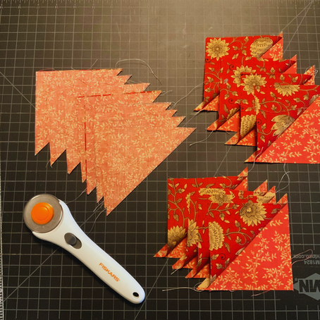 Fabric triangles with floral patterns on a black grid cutting mat. A rotary cutter and measurement lines are visible.
