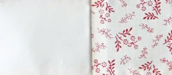 One white quilt fabric square and one white with red print quilt fabric square joined right sides together with a quarter-inch seam