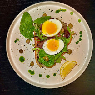 Avocado toast with salted salmon, soft-boiled egg, capers, microgreens and herb oil on sourdough.