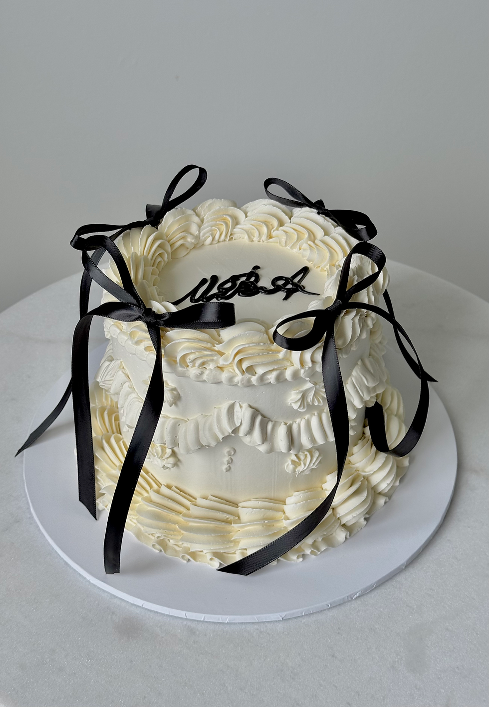 Elegant white birthday cake decorated with piped cream details and black ribbon bows