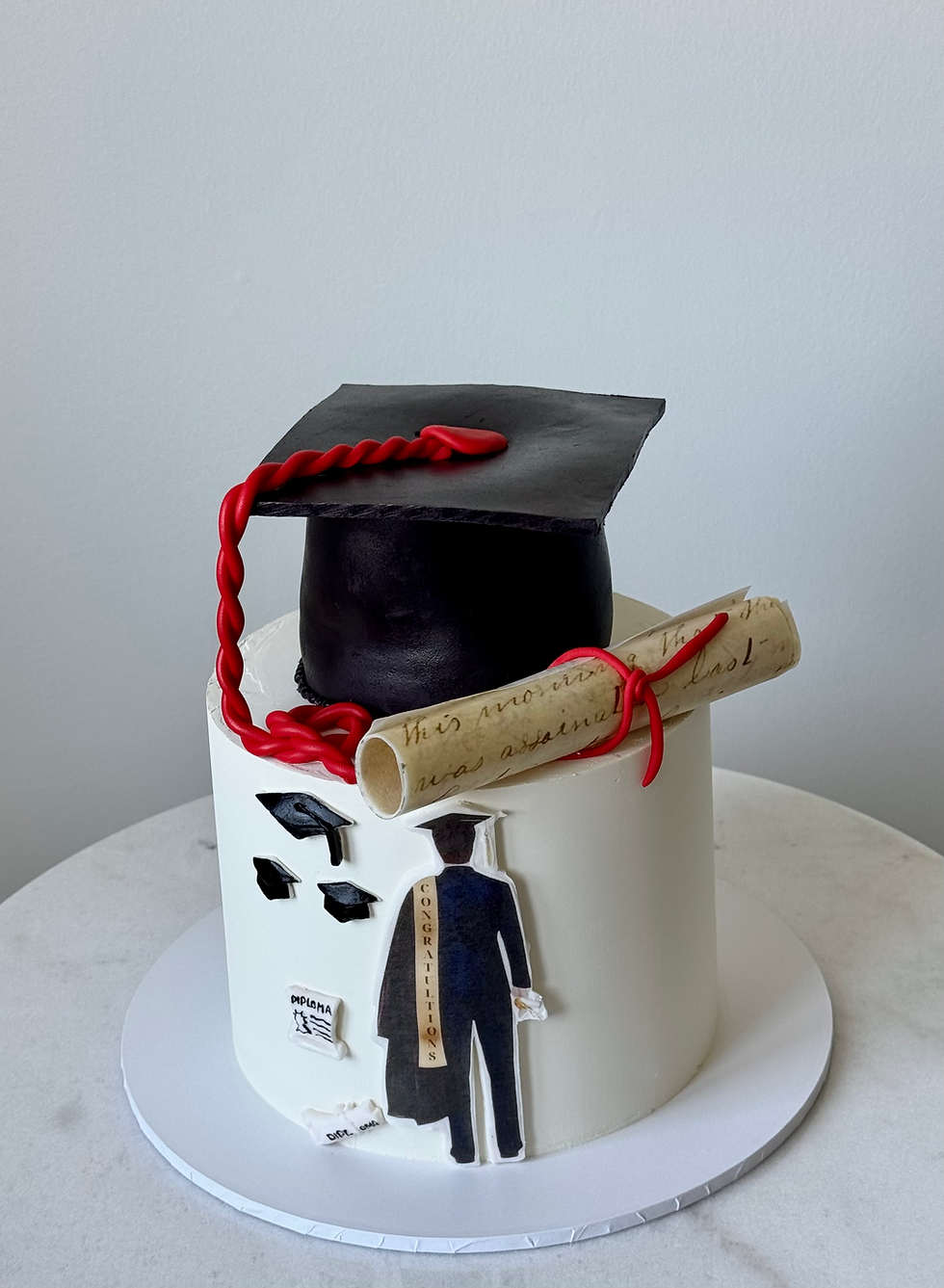 “Graduation cake with black mortarboard cap, diploma scroll, and elegant white finish”