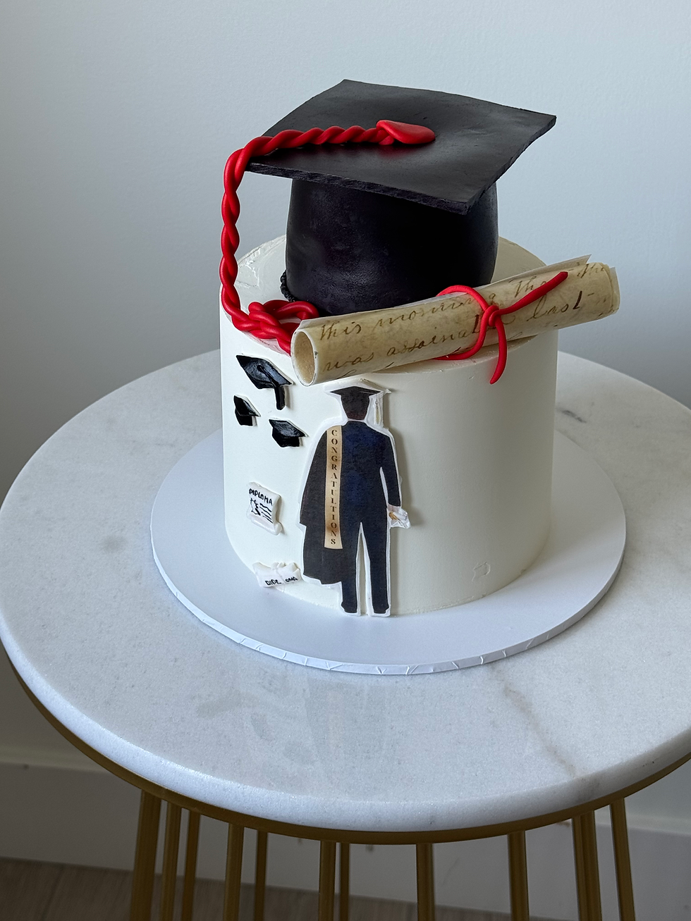 “Graduation cake with black mortarboard cap, diploma scroll, and elegant white finish”